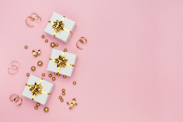 White gift boxes, golden decorations and ornaments on pastel pink background.