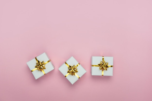 White gift boxes with golden bows on pastel pink background Flat lay top view copy space