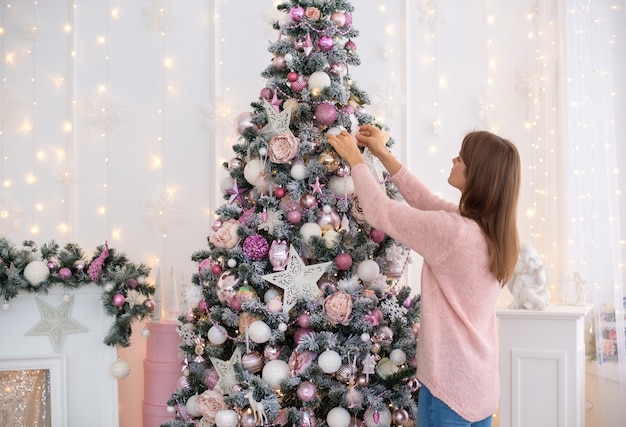 White girl in a knitted dress pink decorates a Christmas tree with Christmas toys