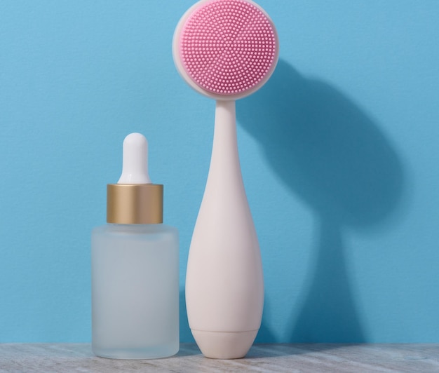 White glass bottle with a pipette and a plastic facial brush on a blue background