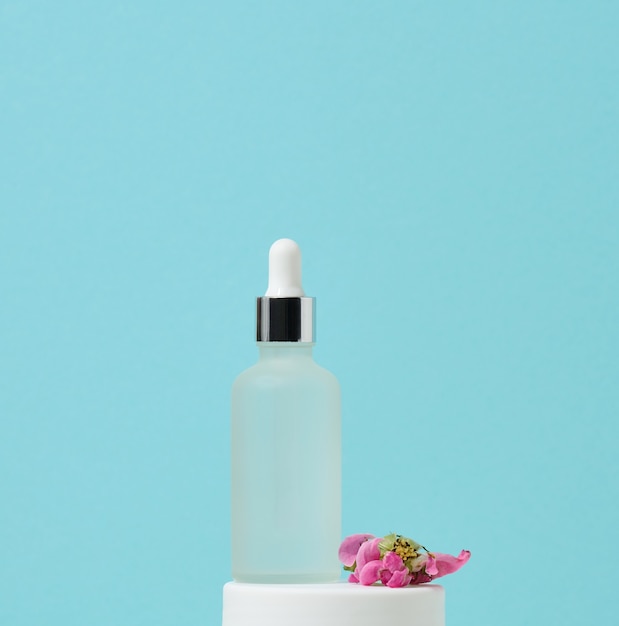 White glass bottle with pipette stands on a blue background. Cosmetics SPA branding. Packaging for gel, serum, advertising and product promotion, mock up