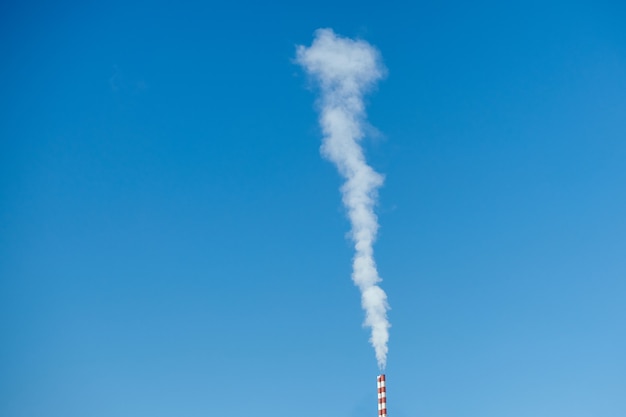 White-gray smoke is polluting from chimney in blue sky in sunny day