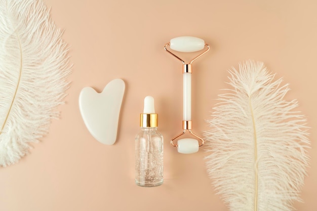 A white Guasha face massager and a face serum lying on a beige background