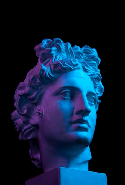 White gypsum copy of ancient statue of Apollo God of Sun head for artists isolated on a black background. Plaster sculpture of man face. Toned blue and purple.