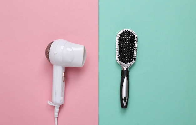 White hair dryer and brush on pink blue background Beauty concept Hair care hair style Top view Flat lay