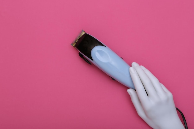 White hand of a mannequin holding a hair clipper on a pink background. Beauty and fashion