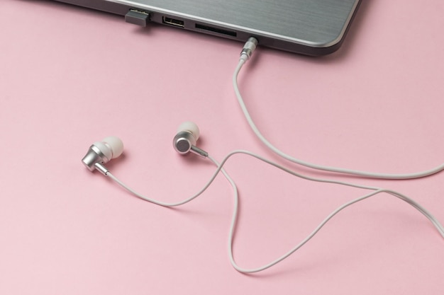 White headphones connected to a laptop on a pink background