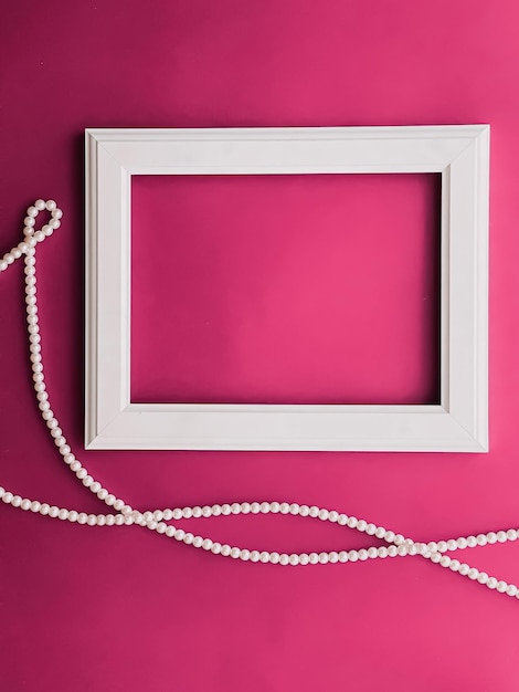 White horizontal art frame and pearl jewellery on pink background as flatlay design artwork print or photo album