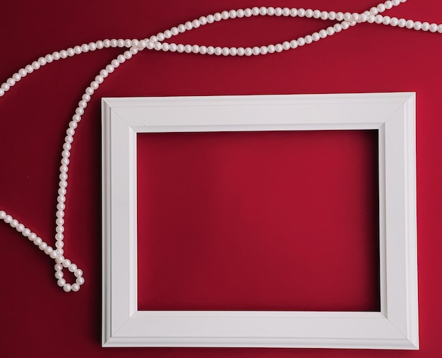 White horizontal art frame and pearl jewellery on red background as flatlay design artwork print or photo album concept