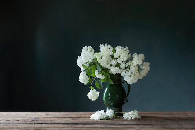 White hydragea in vintage jug on wooden table on background dark wall