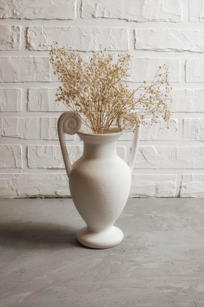 White interior vase with dried flowers against brick wall