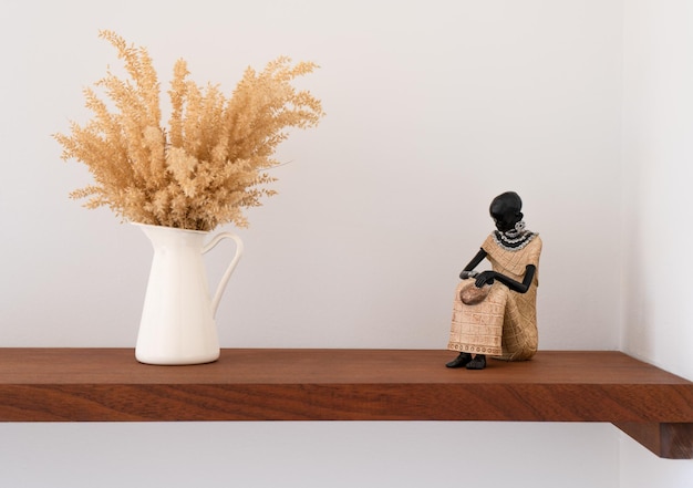 White jar with a plant on a shelf next to a black woman figure