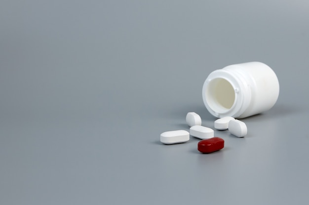 A white jar with scattered pills on a gray background