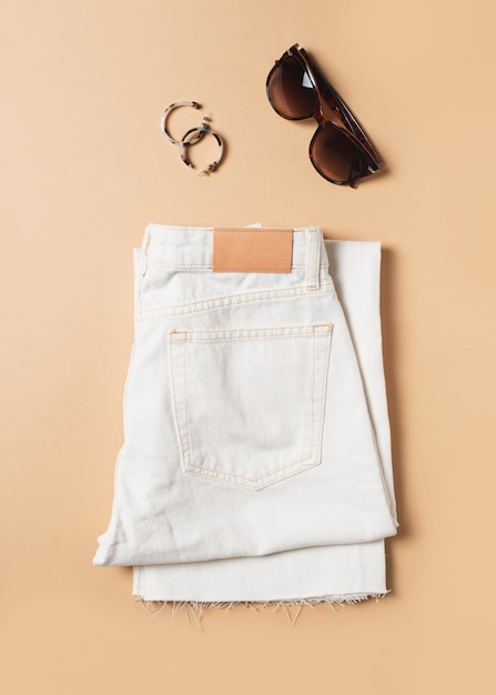 White jeans and denim fashion flat lay with accessories on beige