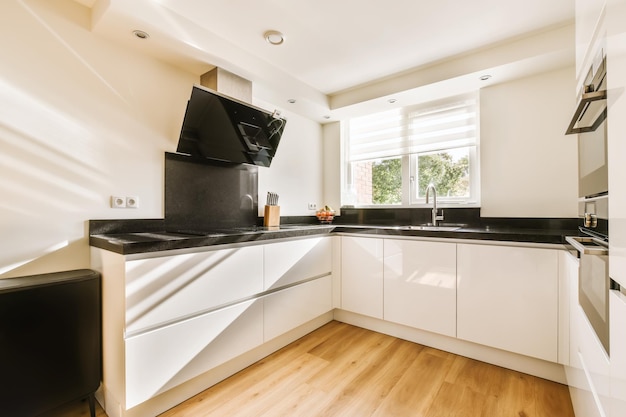 A white kitchen with black counter tops and a window