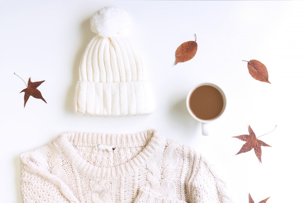 White knitted sweater , wool hat , a cup of coffee and dried maple leaves on a white blackground, flat lay