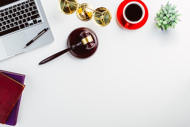 White lawyer desk with laptop, book, pen, cup of coffee, judges gavel and Law symbols.