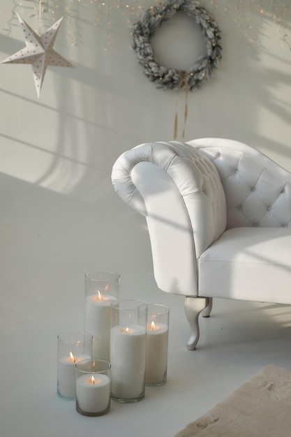 White leather sofa in room decorated with New Year's decor eco fur on floor pillar candles in vases Christmas wreath on the wall