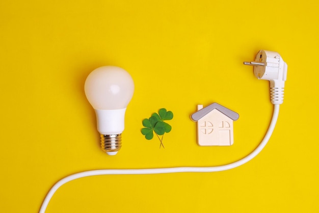 White LED light bulb electric plug leaf and a house symbol on yellow background Concept of save e