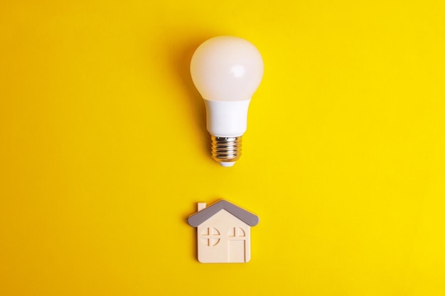 Photo white light bulb and a house symbol on yellow background concept saving energy with led lamp at hom