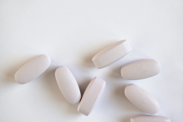 White or light grey long vitamins or pills on white background, macro, close-up, copy space, flatly. Nutritional supplements concept, health, vitamins, monochrome minimal style. Horizontal.