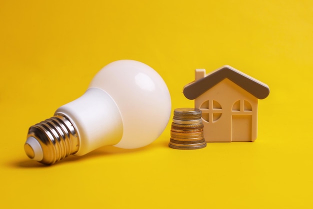 White lightbulb stacked coins and a house miniature over yellow background Concept of saving energ