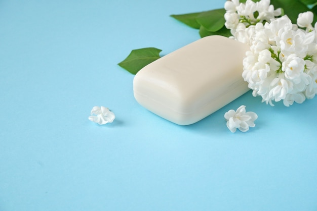 White lilac flowers and soap on blue background natural cosmetic concept