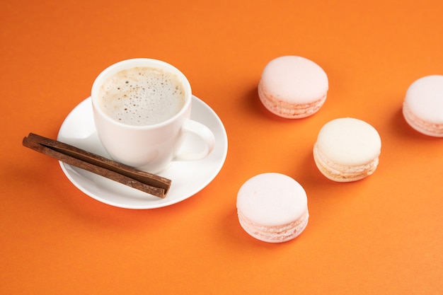 White macarons and coffee with cinnamon on an orange surface