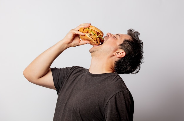 White man in black T-shirt with burger on white wall