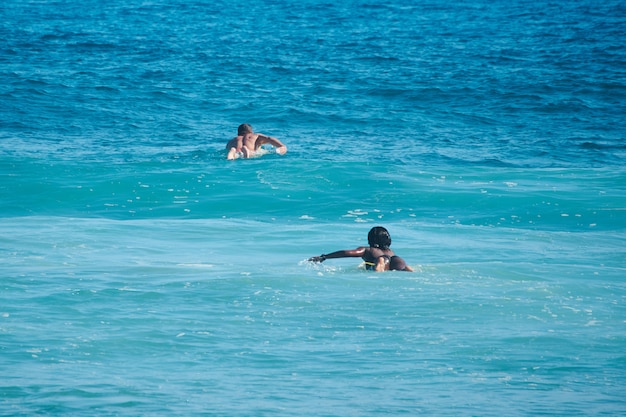 White man and black woman surfers swim on line up. Back view. Lifestule.