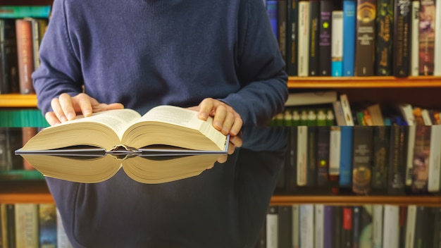 White man reading book at a glass table and bookstore with lots of books.