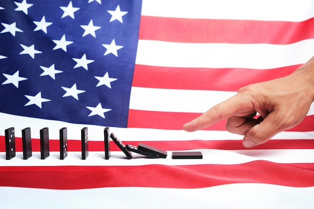 White man's finger pushing a Domino causing a chain reaction against background of the us flag.