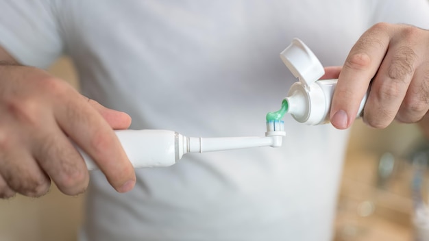 White man's hands pouring thootpaste into an electric toothbrush