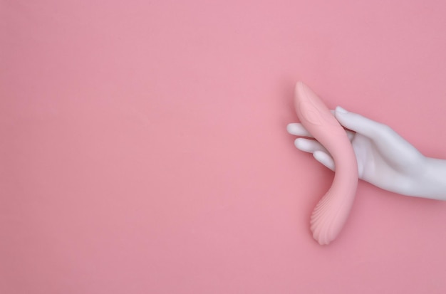 White mannequin hand holding female sex toy on pink pastel background. Top view. Minimalism