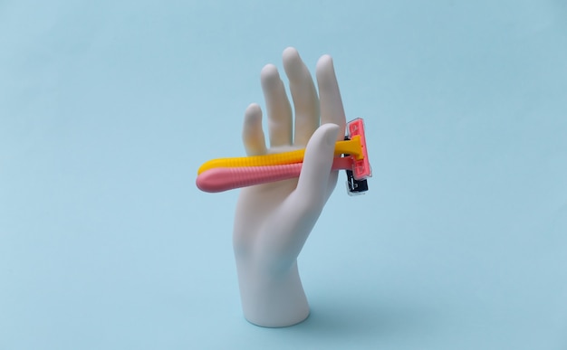 White mannequin hand holds razor epilators on blue background. Beauty, personal care concept