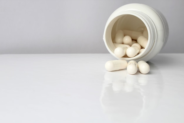 White medical pills and tablets spilling out of a drug bottle.