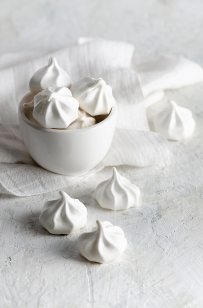 White meringue cookies in a white bowl with a white napkin, on white background.