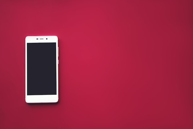 White mobile phone on red background. Digital device with black screen. Branding mock up.