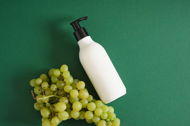 White mock up bottle with dispenser and grapes on green background