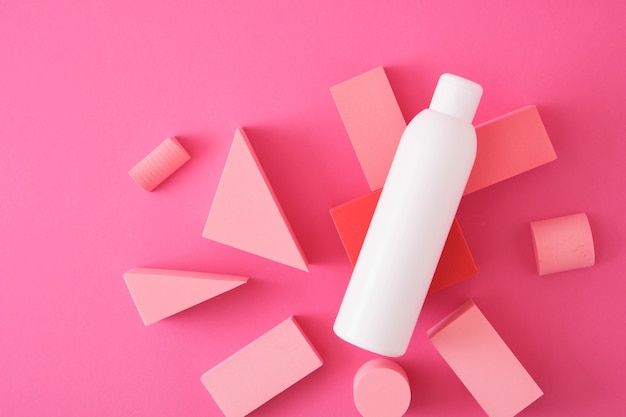 White mock up bottle with shampoo or shower gel and geometric shapes forms. Exhibition podium, platform for product presentation on pink background. top view