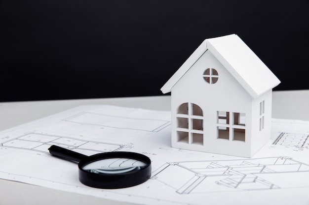 White model of house and a magnifying glass on a drawing real estate building concept