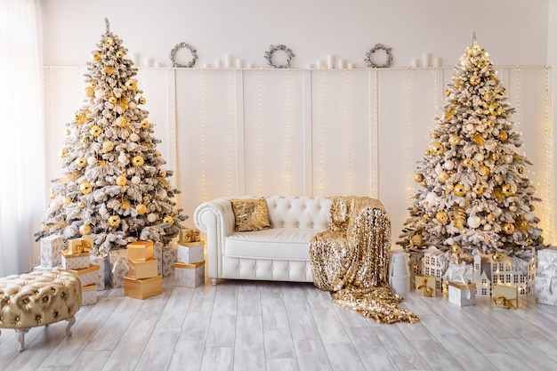 White modern christmas interior with new year trees decorated gold pouf textile presents