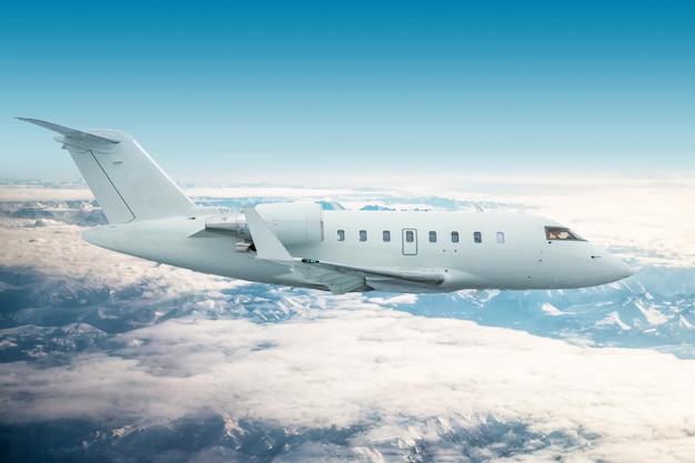 White modern executive jetliner flies over snow covered mountains