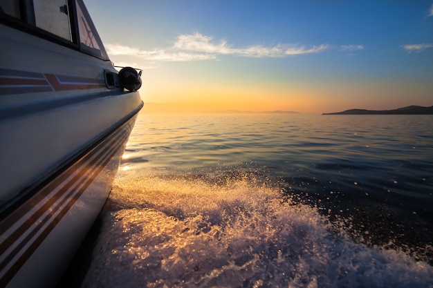 White motorboat moving fast to sunset