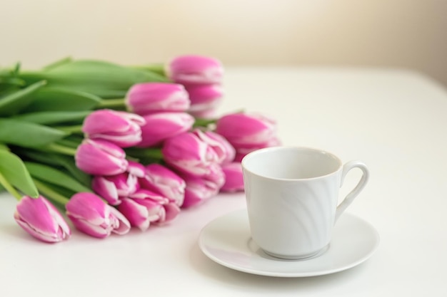 A white mug and a bouquet of beautiful pink tulips on white table