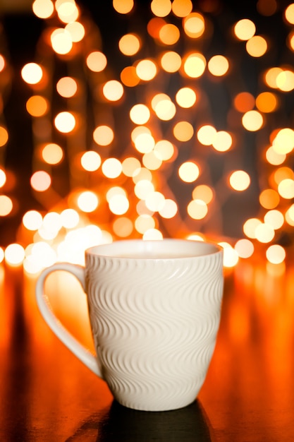 Photo white mug on the dark brown table and background with golden bokeh