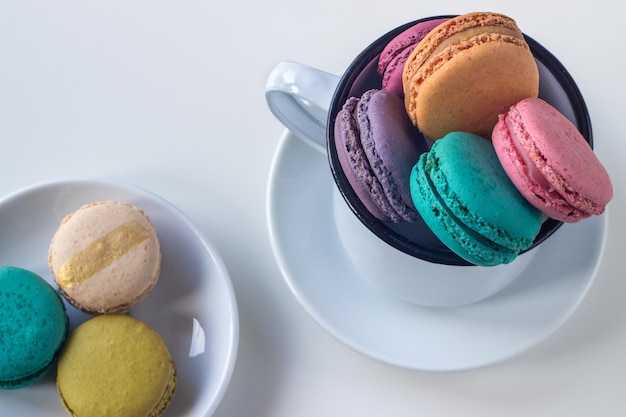 White mug full of colorful macaroons on light background. Copy space. Selective focus.