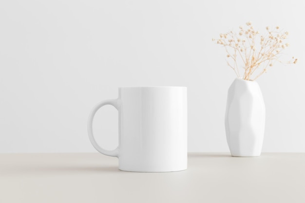 Photo white mug mockup with a gypsophila in a vase on a beige table