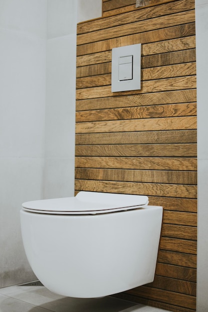 Photo white new toilet and metallic button mounted on the wall against a background of stylish wood tiles