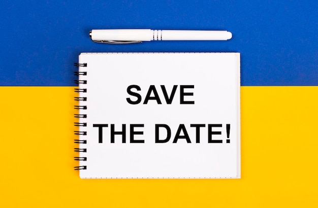 A white notebook with the text SAVE THE DATE and a white pen on a blue and yellow background